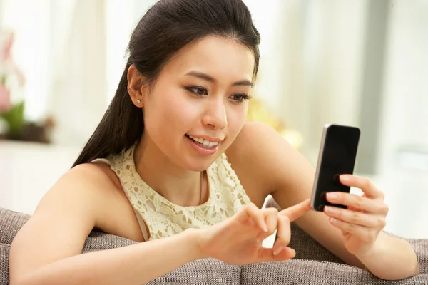 Jovem chinesa usando telefone celular no sofá em casa — Fotografia de Stock