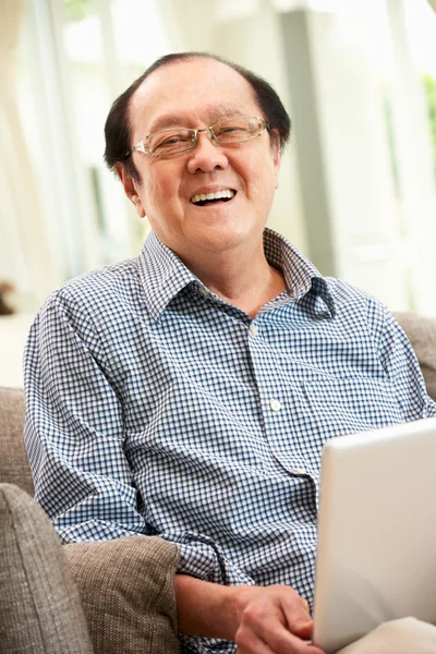 自宅のソファでリラックスしながら、ラップトップを使用して上級中国人の男 — ストック写真