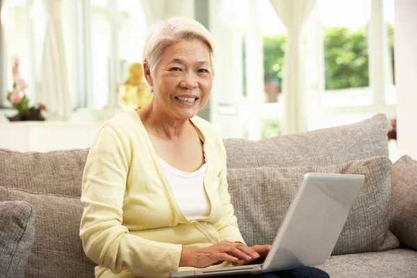 Mulher chinesa sênior usando laptop enquanto relaxa no sofá no Hom — Fotografia de Stock