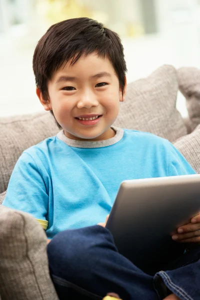 Chico joven chino usando Tablet Computer mientras está sentado en el sofá A —  Fotos de Stock