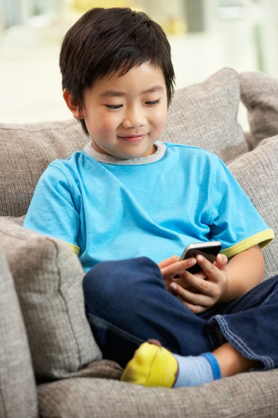 Junger chinesischer Junge benutzt Handy auf Sofa zu Hause — Stockfoto