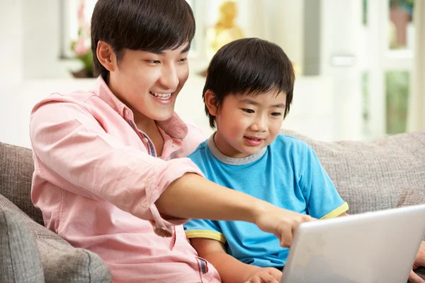 Padre e figlio cinese che usano il computer portatile mentre si rilassano sul divano a H — Foto Stock