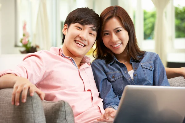 Unga kinesiska par använder laptop medan du kopplar av på soffan på hom — Stockfoto
