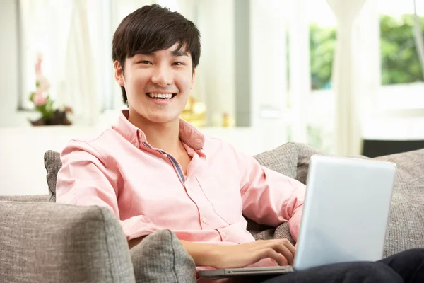 Young Chinese Man Using Laptop Whilst Relaxing On Sofa At Home — Stock Photo, Image