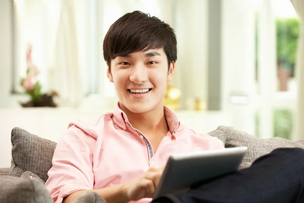 Genç Çinli adam kanepede rahatlatıcı ederken dijital tablet kullanarak bir — Stok fotoğraf