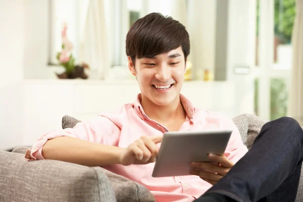 Jovem chinês usando tablet digital enquanto relaxa no sofá A — Fotografia de Stock