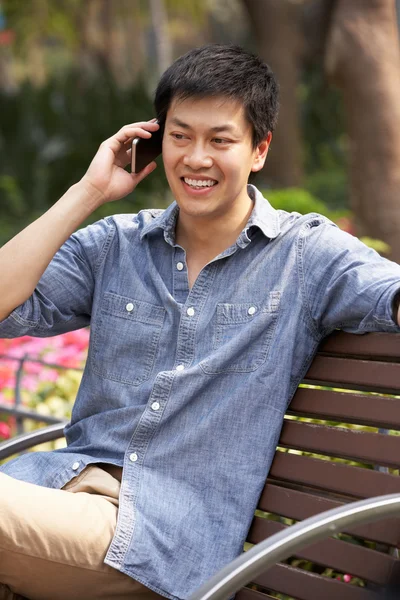 Jonge chinese man ontspannen op een bankje praten op mobiele telefoon — Stockfoto