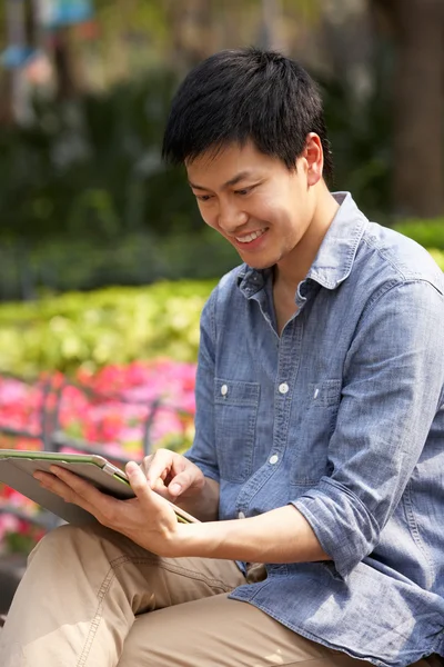 Homem chinês jovem usando tablet digital enquanto relaxa no parque — Fotografia de Stock