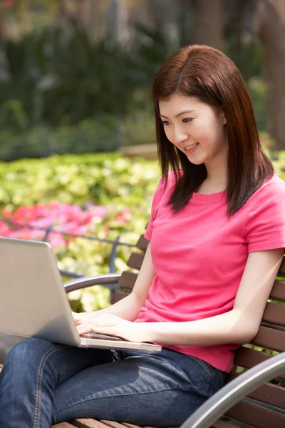 Joven mujer china usando el ordenador portátil mientras se relaja en el banco del parque — Foto de Stock