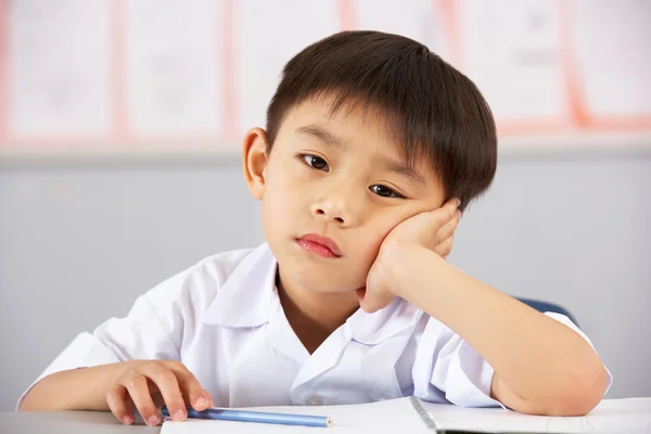 Unhappy Male Student Working At Desk In Chinese School Classroom Stock Image