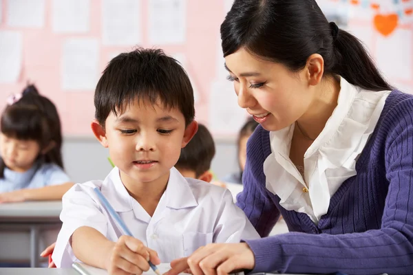 Profesor ayudando a estudiante a trabajar en el escritorio en la escuela china Classr Fotos de stock libres de derechos