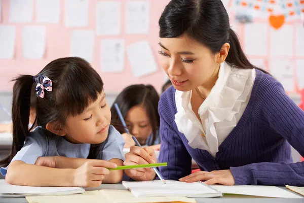 Profesor ayudando a estudiante a trabajar en el escritorio en la escuela china Classr Fotos De Stock Sin Royalties Gratis