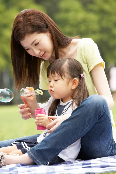 Chinese Mother With Daughter In Park Blowing Bubbles Stock Photo