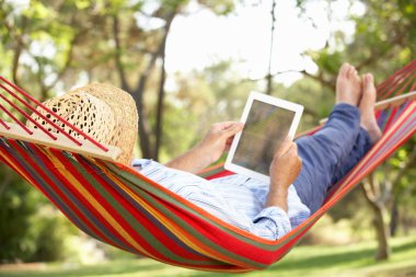 Senior Man Relaxing In Hammock With E-Book clipart