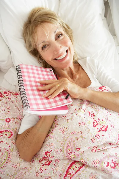 Ανώτερος γυναίκα ξεκούραστη στο κρεβάτι ανάγνωση ημερολόγιο — Φωτογραφία Αρχείου
