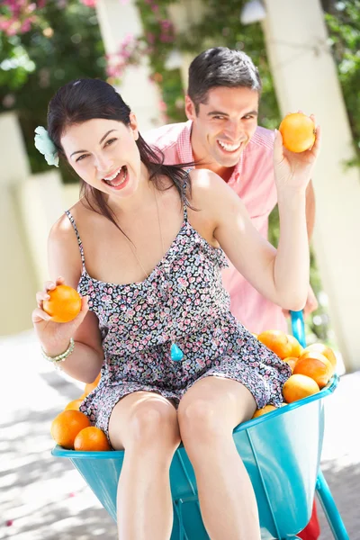 Homem empurrando mulher no carrinho de mão preenchido com laranjas — Fotografia de Stock