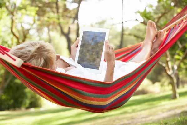 Senior vrouw ontspannen in een hangmat met e-boek — Stockfoto