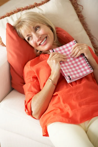 Seniorin sitzt auf Sofa und liest Tagebuch — Stockfoto