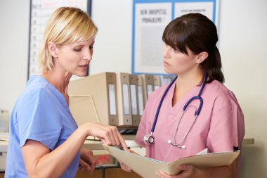 Two Nurses Discussing Patient Notes At Nurses Station clipart