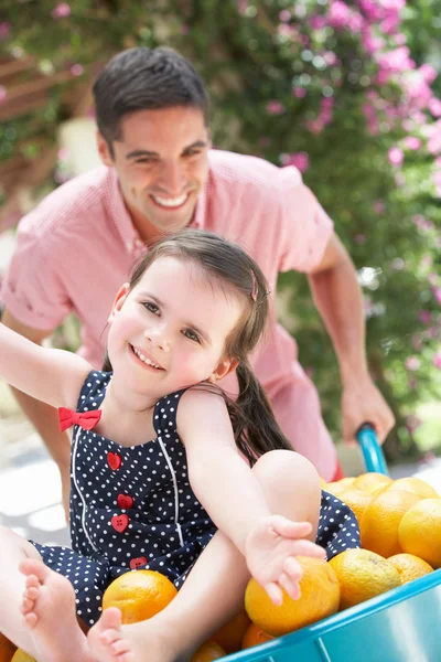 Vader dochter duwen in kruiwagen gevuld met sinaasappelen — Stockfoto