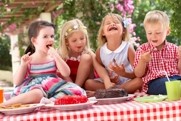 Skupina dětí jíst želé a dort na venkovní tea party — Stock fotografie