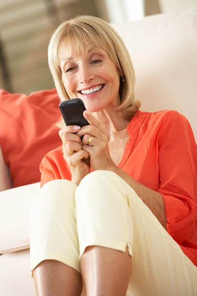 Senior mulher relaxante no sofá enviando mensagem de texto — Fotografia de Stock