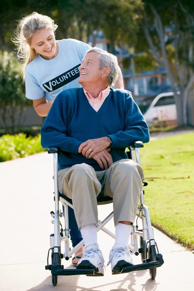 Dospívající dobrovolníků tlačí starší muž na invalidním vozíku — Stock fotografie