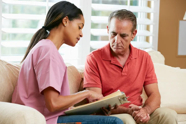 Enfermera debatiendo sobre registros con paciente masculino senior en casa vi — Stockfoto