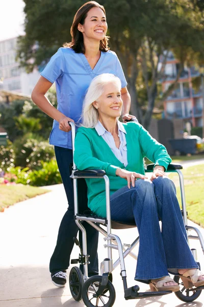 Opiekun pchanie starszy kobieta na wózku inwalidzkim — Zdjęcie stockowe