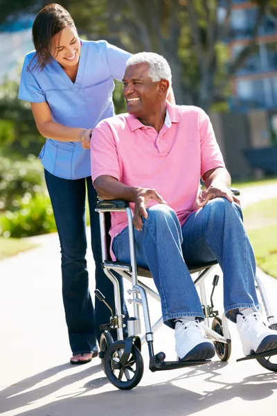 Cuidador empurrando o homem sênior na cadeira de rodas — Fotografia de Stock