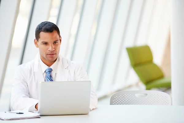 Médico usando laptop sentado na mesa no hospital moderno — Fotografia de Stock