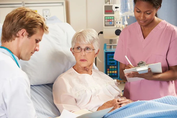 Arzt mit Krankenschwester im Gespräch mit Seniorin im Bett — Stockfoto