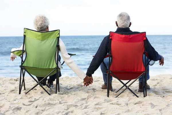 Старшая пара, сидящая на пляже в шезлонгах — стоковое фото