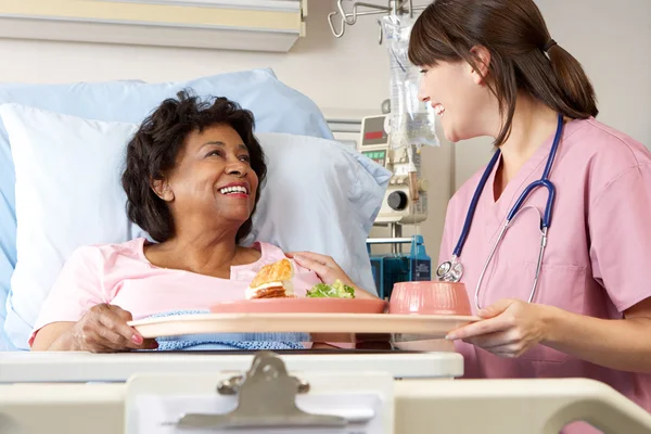 Verpleegkundige serveren senior vrouwelijke patiënt maaltijd in ziekenhuisbed — Stockfoto