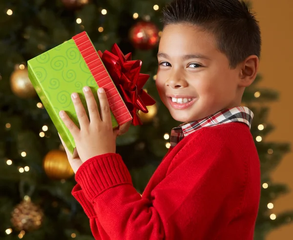 Boy Holding Christmas Present In Front Of Tree — Stock Photo, Image