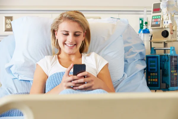 Teenage kvinnlig patient med mobiltelefon i sjukhussäng — Stockfoto