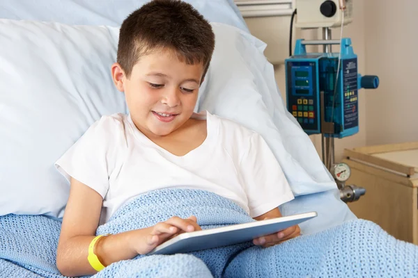 Menino que relaxa na cama do hospital com tabuleta digital — Fotografia de Stock