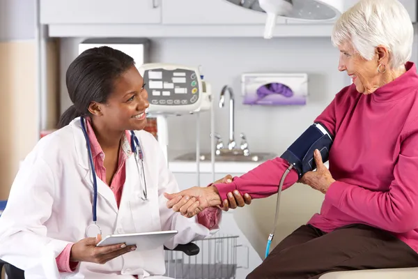 Doktor při starší žena pacientův krevní tlak — Stock fotografie