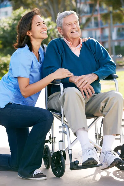 Carer spingendo uomo anziano in sedia a rotelle — Foto Stock