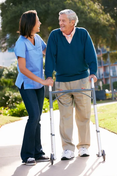 Carer Aiutare l'uomo anziano con telaio a piedi — Foto Stock