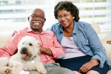 Happy Senior Couple Sitting On Sofa With Dog clipart