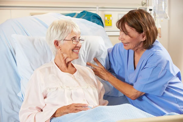 Sjuksköterska talar med ledande kvinnliga tålmodig i sjukhussäng — Stockfoto