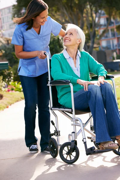 Carer spingendo donna anziana in sedia a rotelle — Foto Stock