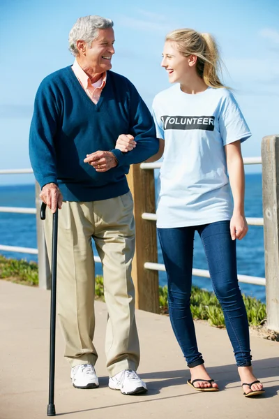 Teenage Volunteer Helping Senior Man Walking Along Path By The S — Stock Photo, Image