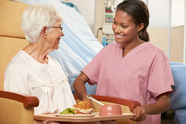 Verpleegkundige portie maaltijd te senior vrouwelijke patiënt zittend in stoel — Stockfoto