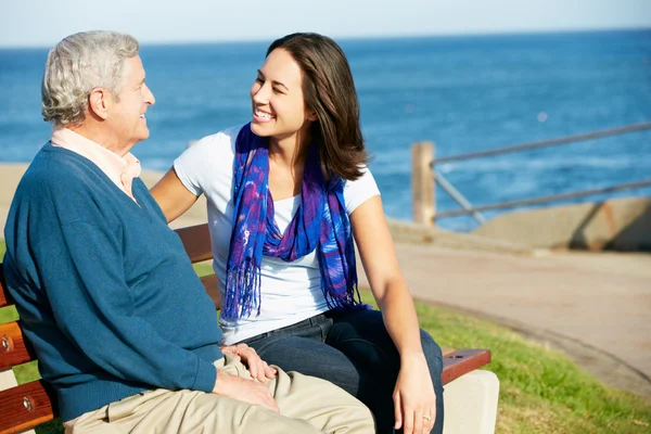 Senior sitzt mit erwachsener Tochter auf Bank am Meer — Stockfoto