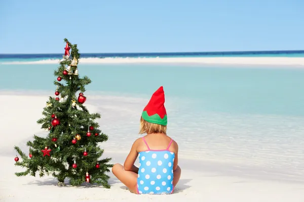 Chica sentada en la playa con árbol de Navidad y sombrero — Foto de Stock