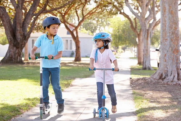 Jongen en meisje dragen veiligheidshelmen en rijden scooters — Stockfoto