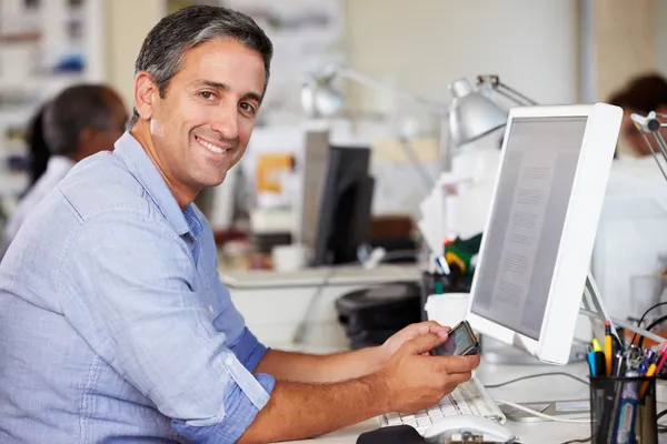 Man använder mobiltelefon på skrivbord i upptagen kreativa kontor — Stockfoto