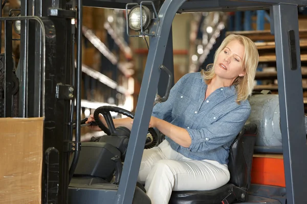 Vrouw drijvende fork lift truck in magazijn — Stockfoto